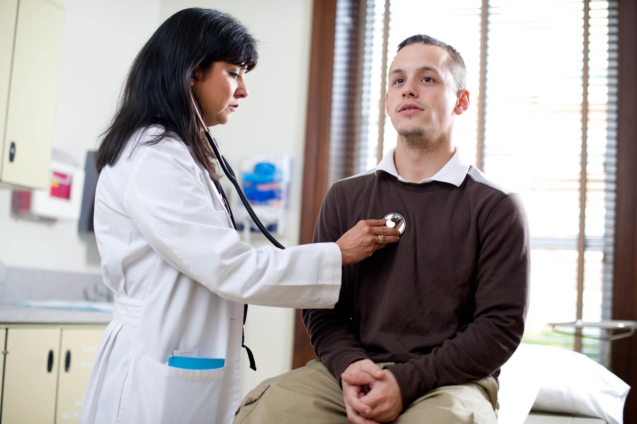 Nurse listening to male patient's heart.