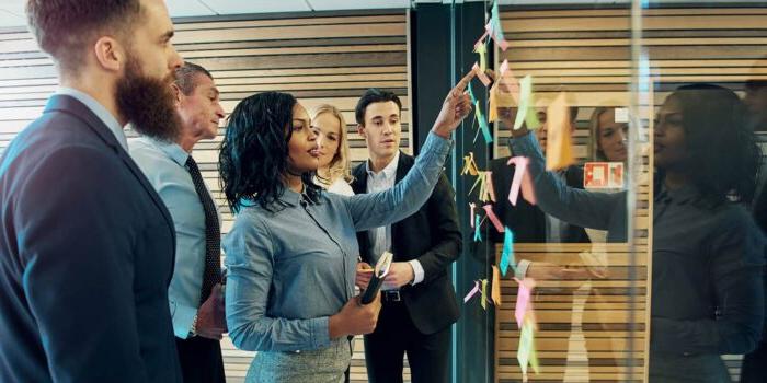 Creative group of business people brainstorming putting sticky notes on glass wall in office.