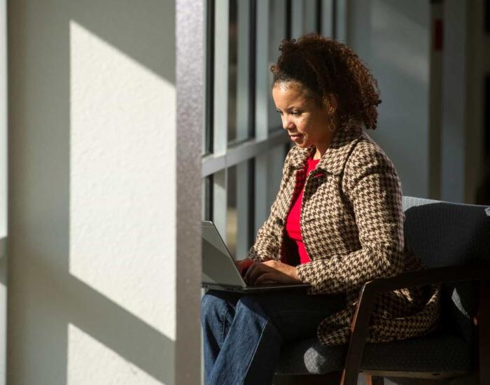 Woman working on a computer sitting by windows.