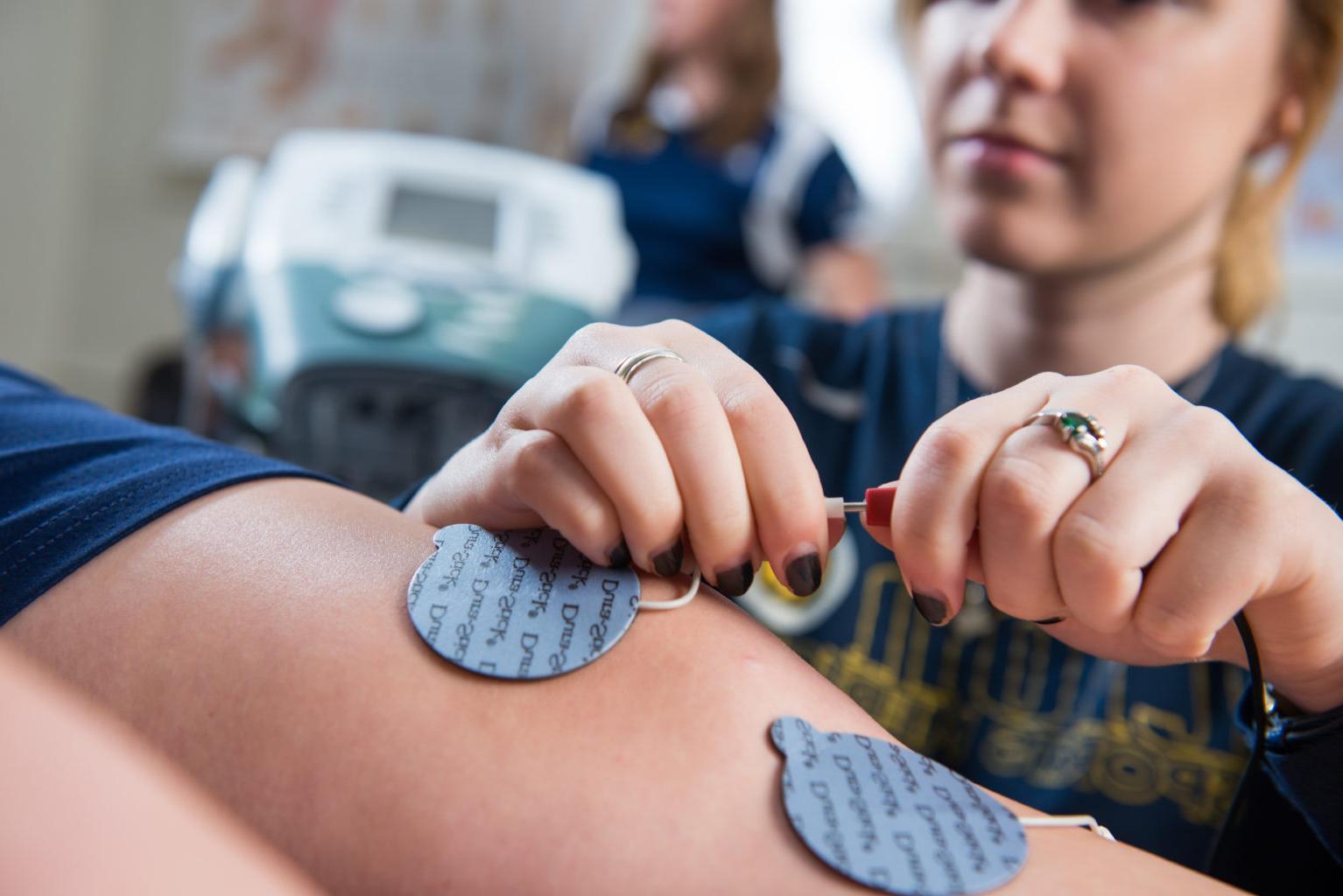 Woman putting electrodes on an athletes legs.