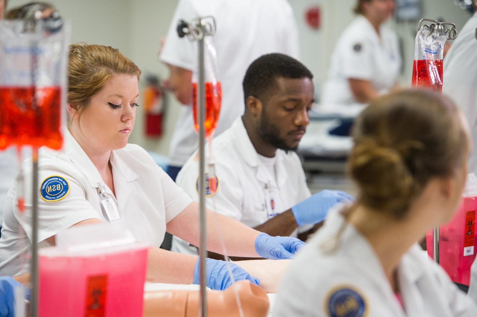 Nurses in classroom with gloves and practicing setting IVs