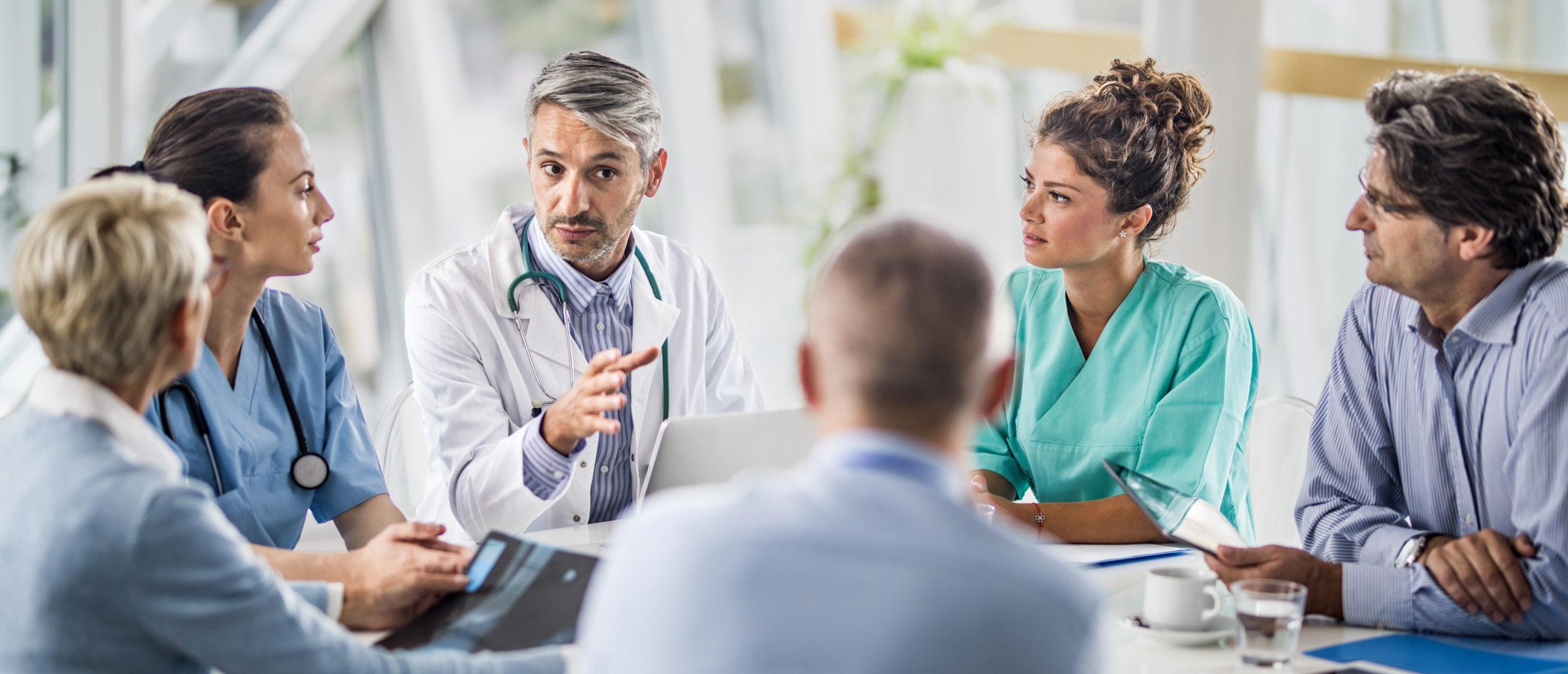 Male doctor and his female colleagues talking to team of business people on a meeting in the hospital.