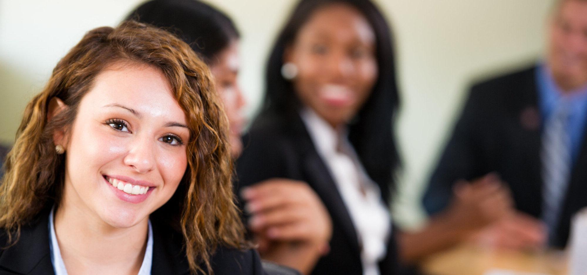 Young lady smiling with other professionally dressed students in the background.