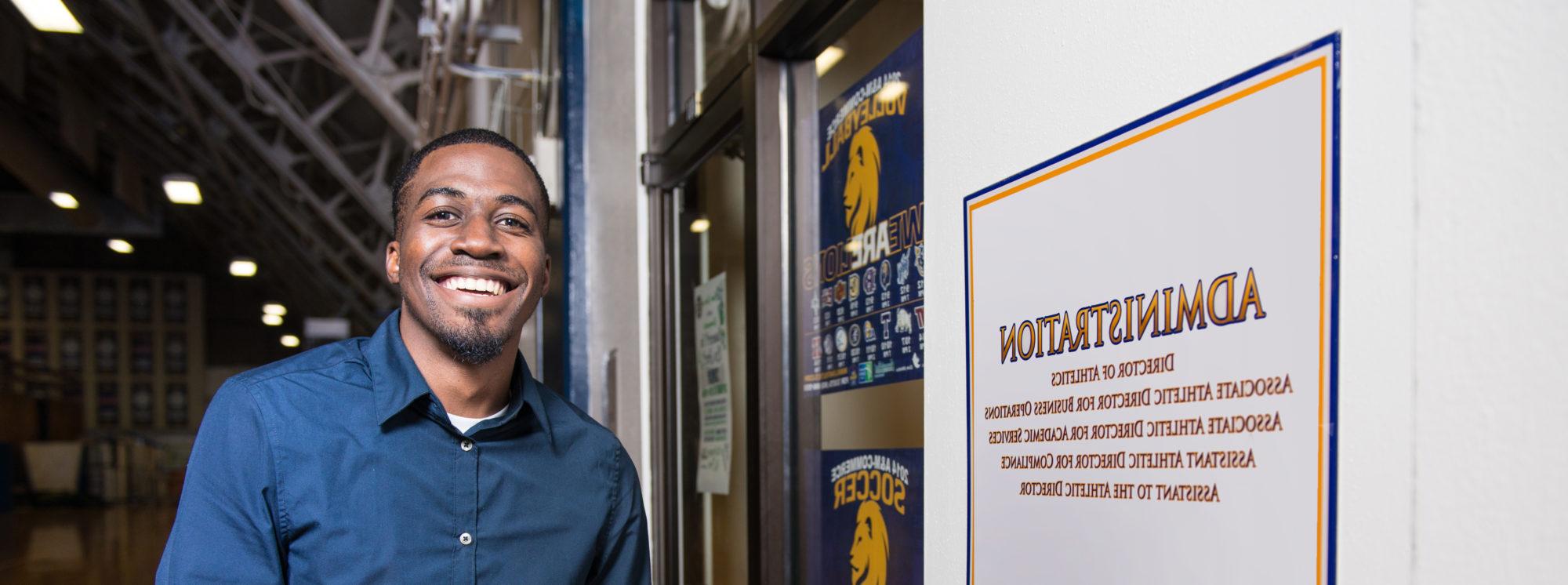 Athletic Administration Student smiling at the camera by the door of the ETAMU Athletics administration department. 